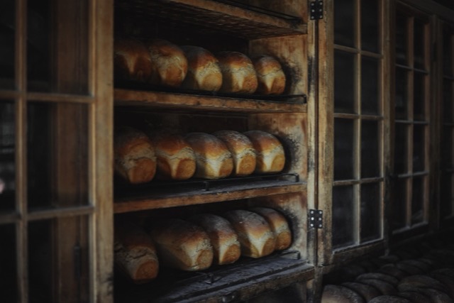 Loaves of bread cooling on wooden shelves in a dim old bakery cupboard
