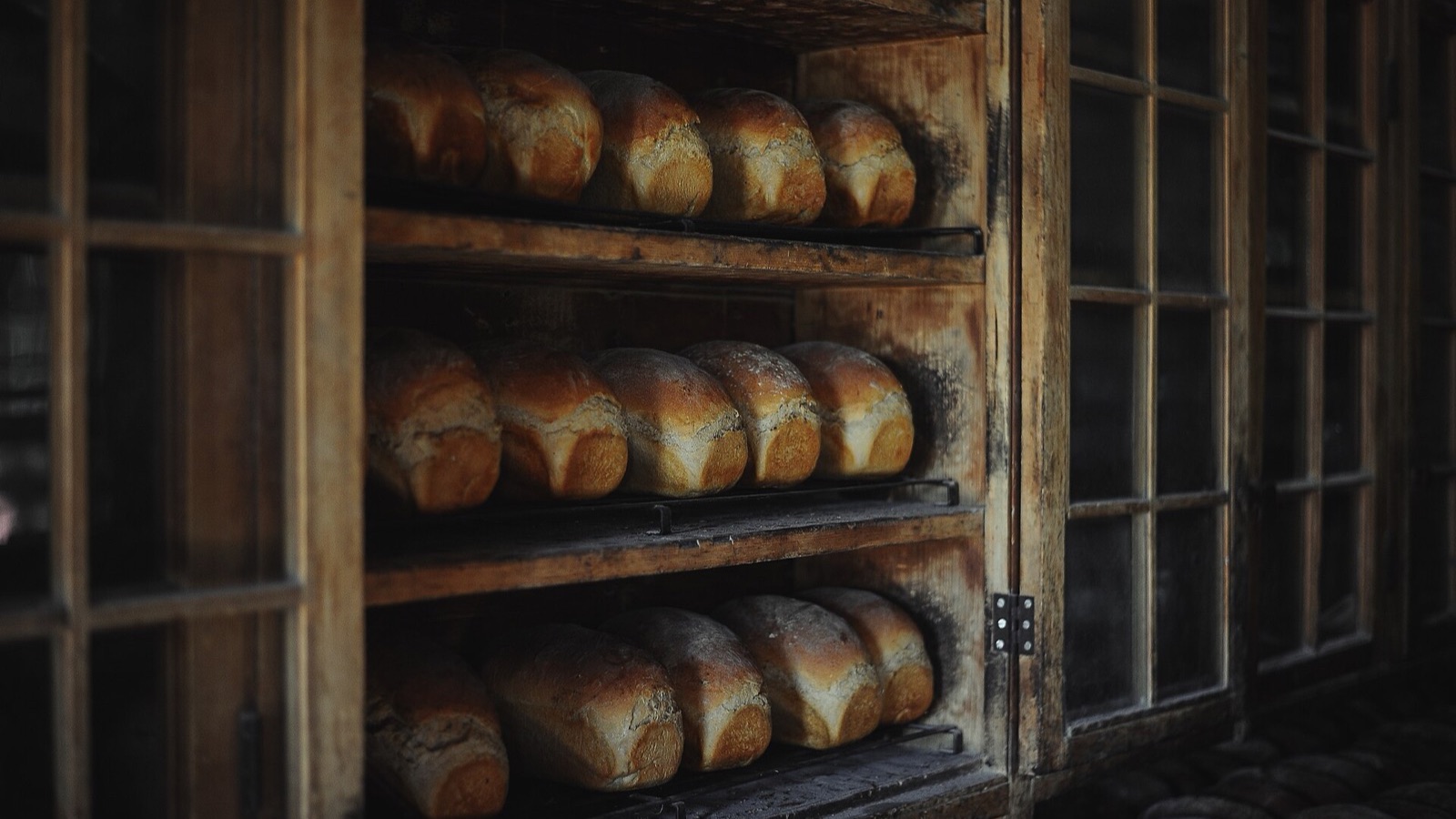 Loaves of bread cooling on wooden shelves in a dim old bakery cupboard