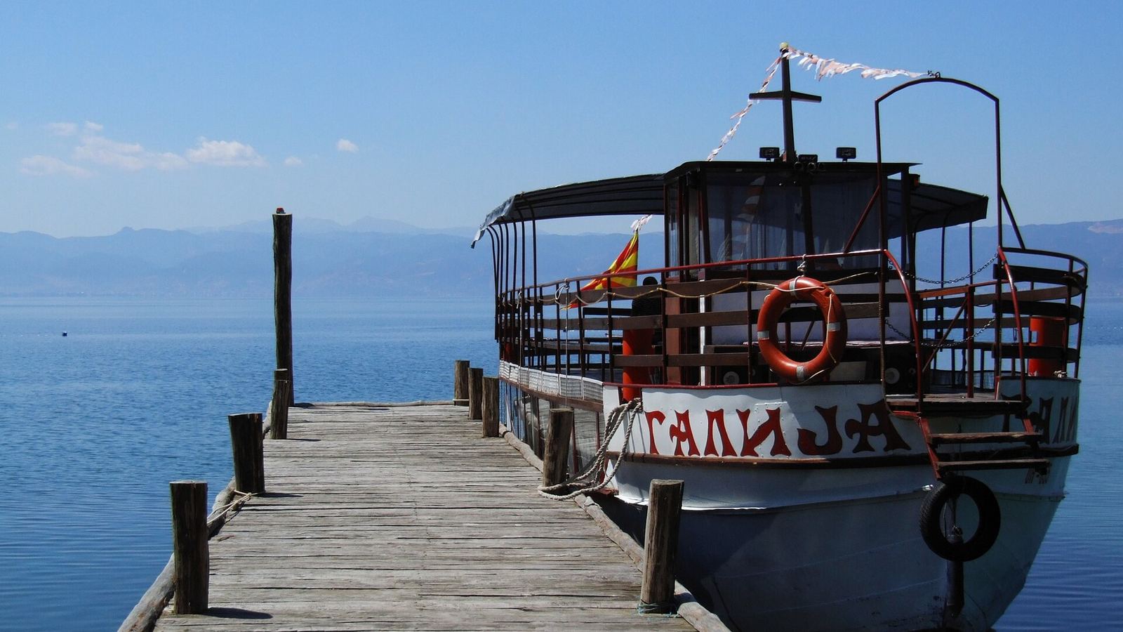 An old wooden boat moored at a wooden jetty on a wide lake