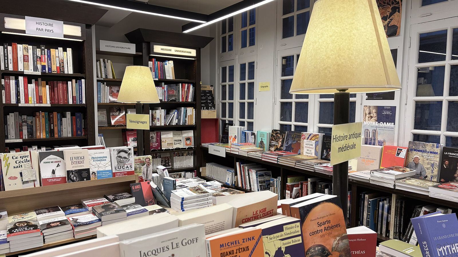Tables of books beneath wide lampshades in a quiet bookshop