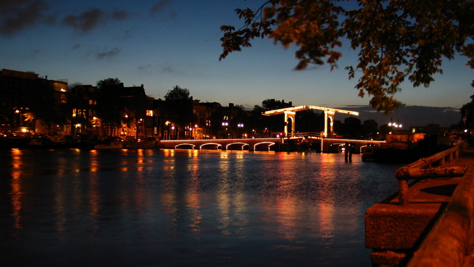 A lifting bridge outlined in lights across a canal at dusk