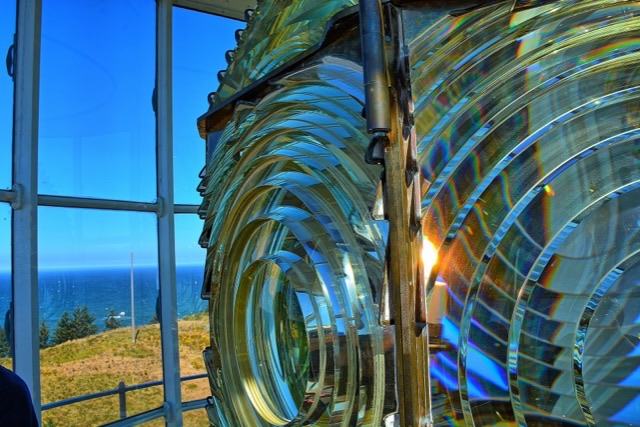 A lighthouse’s great Fresnel lens beside lantern-room windows over a calm sea