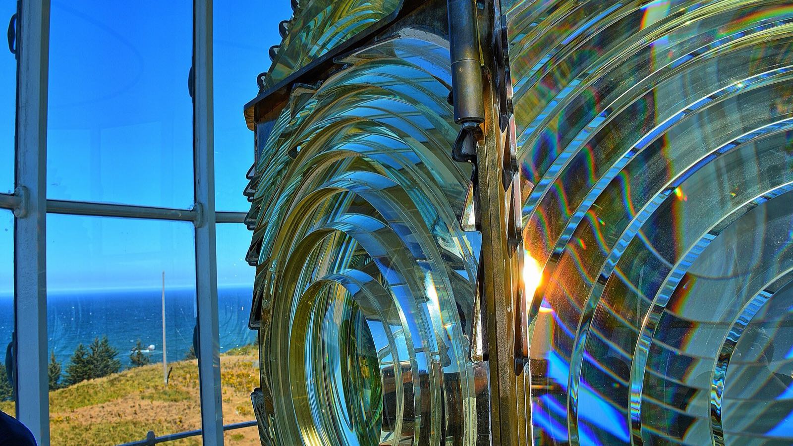 A lighthouse’s great Fresnel lens beside lantern-room windows over a calm sea