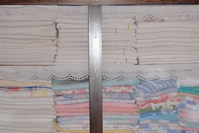 Stacks of folded white sheets and pastel linen on shelves in a wooden cupboard
