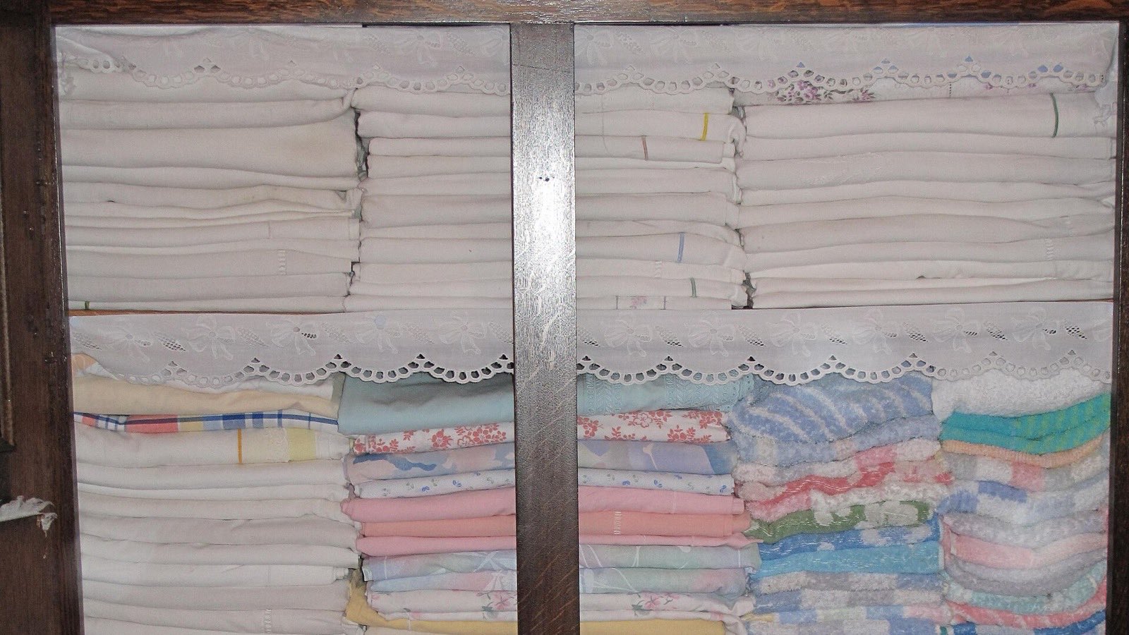 Stacks of folded white sheets and pastel linen on shelves in a wooden cupboard