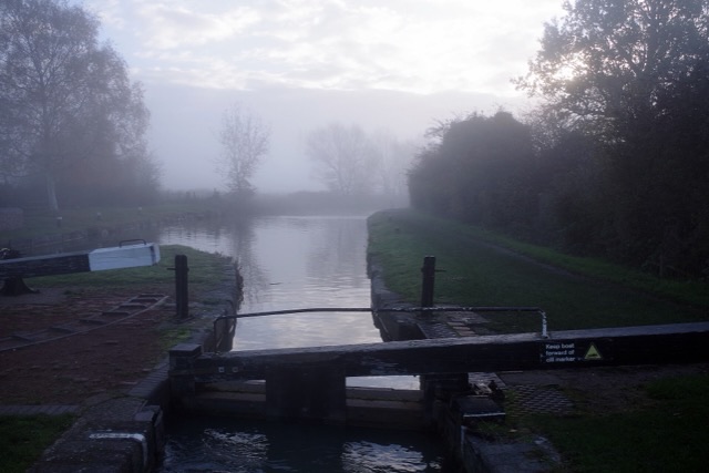 Wooden lock gates over still canal water fading into soft grey mist
