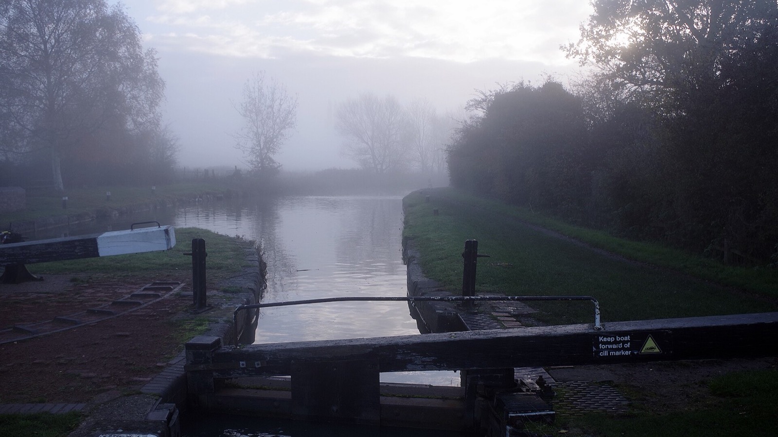 Wooden lock gates over still canal water fading into soft grey mist