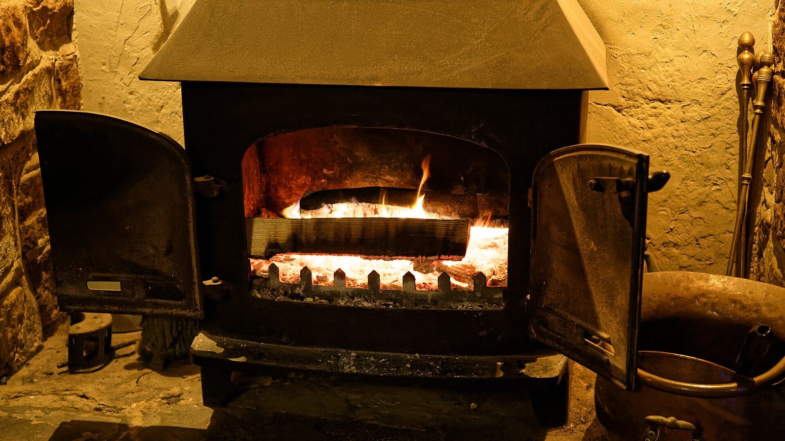 A wood-burning stove alight in a stone hearth