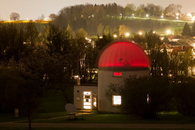 A small observatory at night, its dome glowing red above the trees