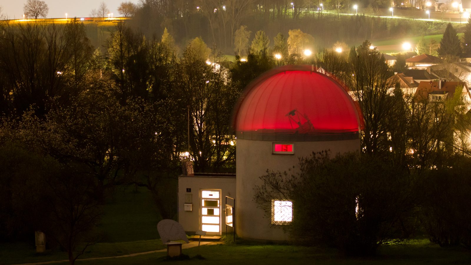 A small observatory at night, its dome glowing red above the trees
