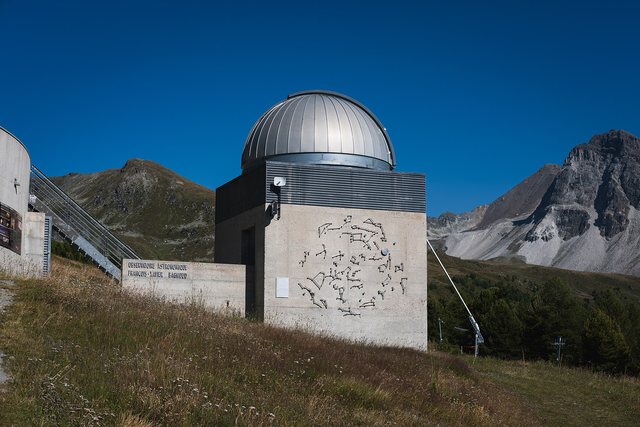 A small hillside observatory with its dome closed beneath bare mountains