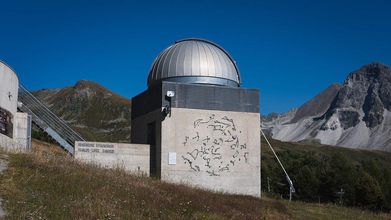 A small hillside observatory with its dome closed beneath bare mountains