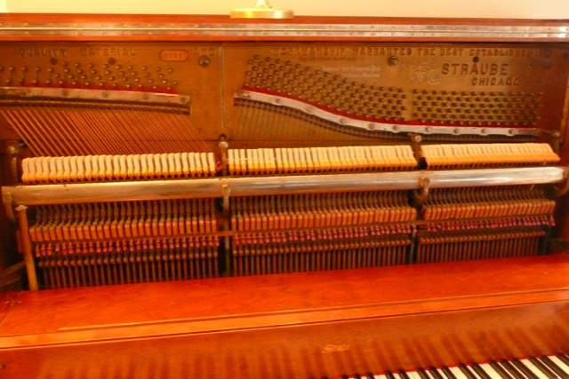 An old upright piano with its front panel off, showing hammers, strings and tuning pins