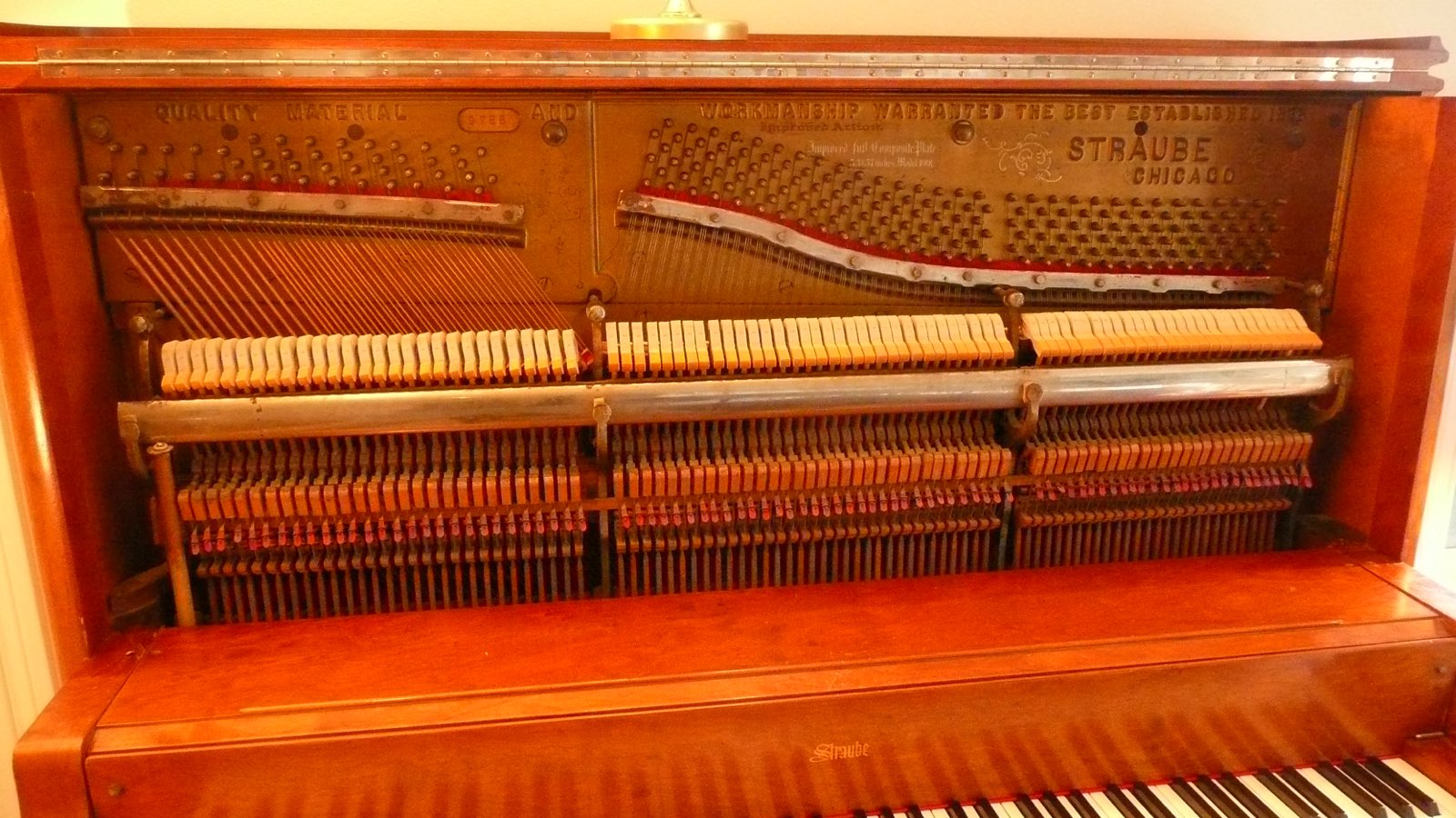 An old upright piano with its front panel off, showing hammers, strings and tuning pins