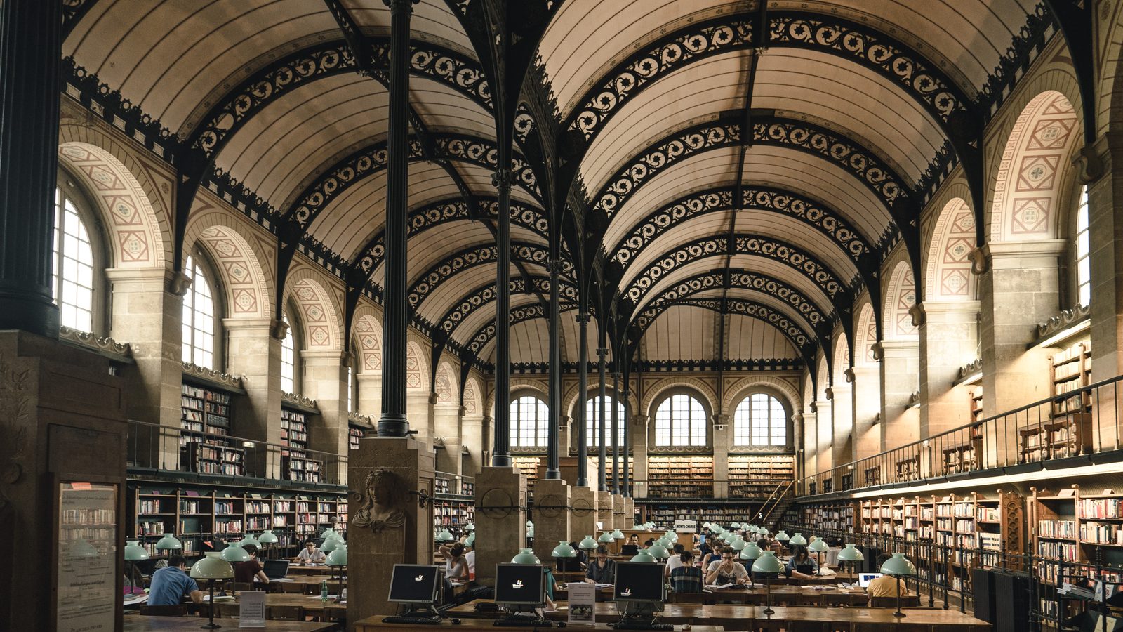 Green lamps along the long tables of a vaulted reading room