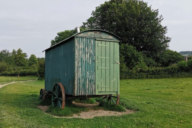 A weathered green shepherd’s hut on iron wheels standing in a grassy pasture