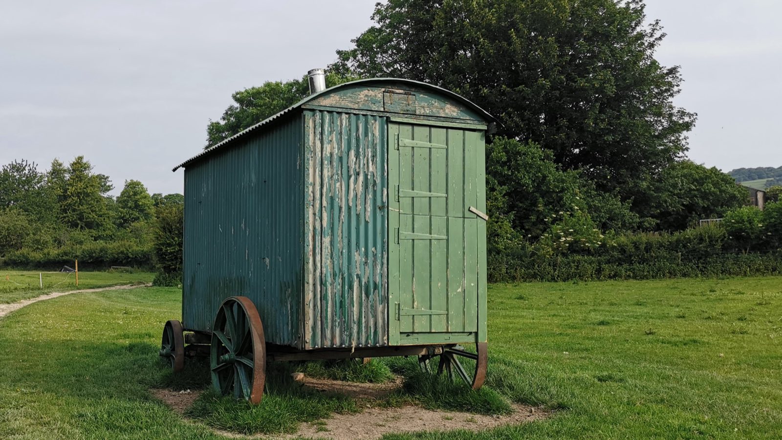 A weathered green shepherd’s hut on iron wheels standing in a grassy pasture