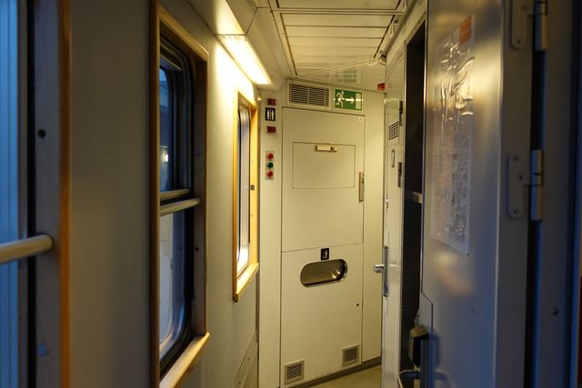 The dim corridor of a sleeping car at night, lit by one lamp