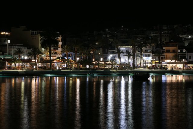 The lit windows of a small harbour town reflected in the water at night