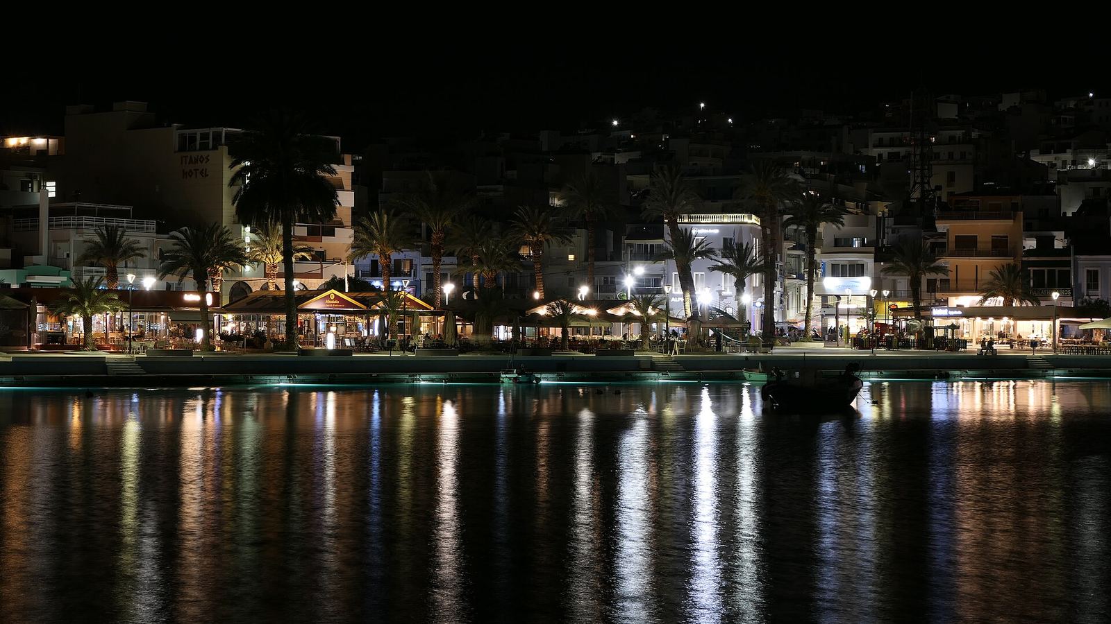 The lit windows of a small harbour town reflected in the water at night