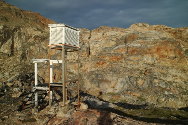 A white louvred instrument screen on a rocky hillside in low evening sun