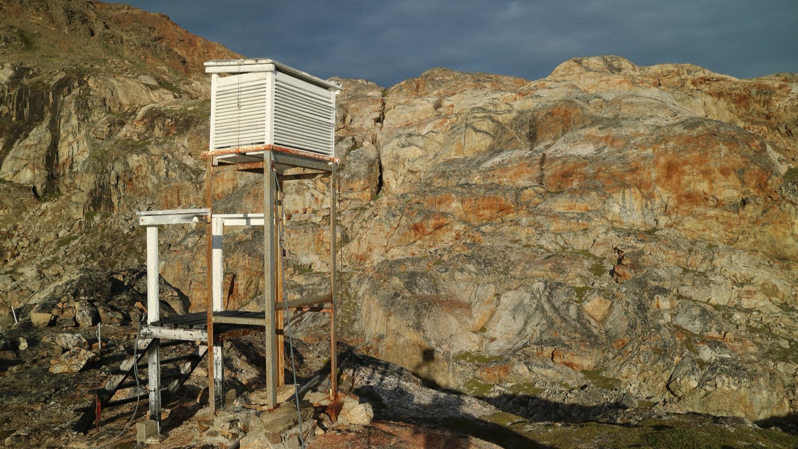 A white louvred instrument screen on a rocky hillside in low evening sun