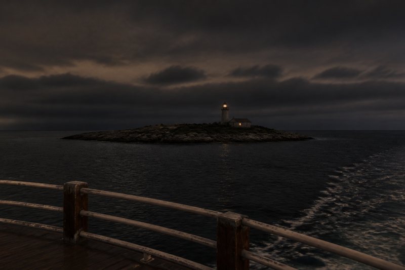 A lighthouse island beyond the wake of a night ferry