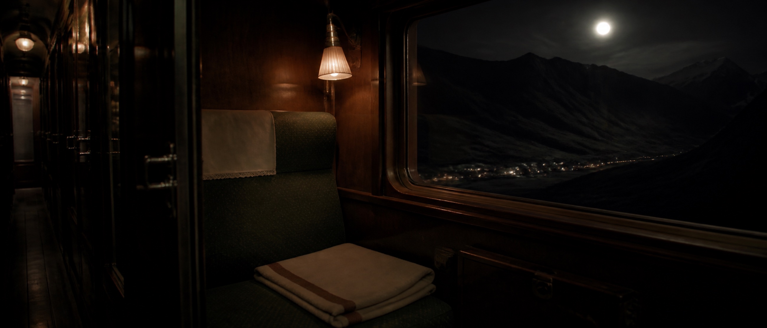 An empty night-train compartment passing a moonlit Alpine valley