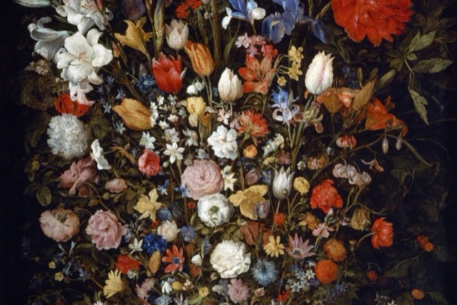 A large bouquet of many kinds of flowers in a round wooden tub on a table, with a few fallen flowers and butterflies on the tabletop.