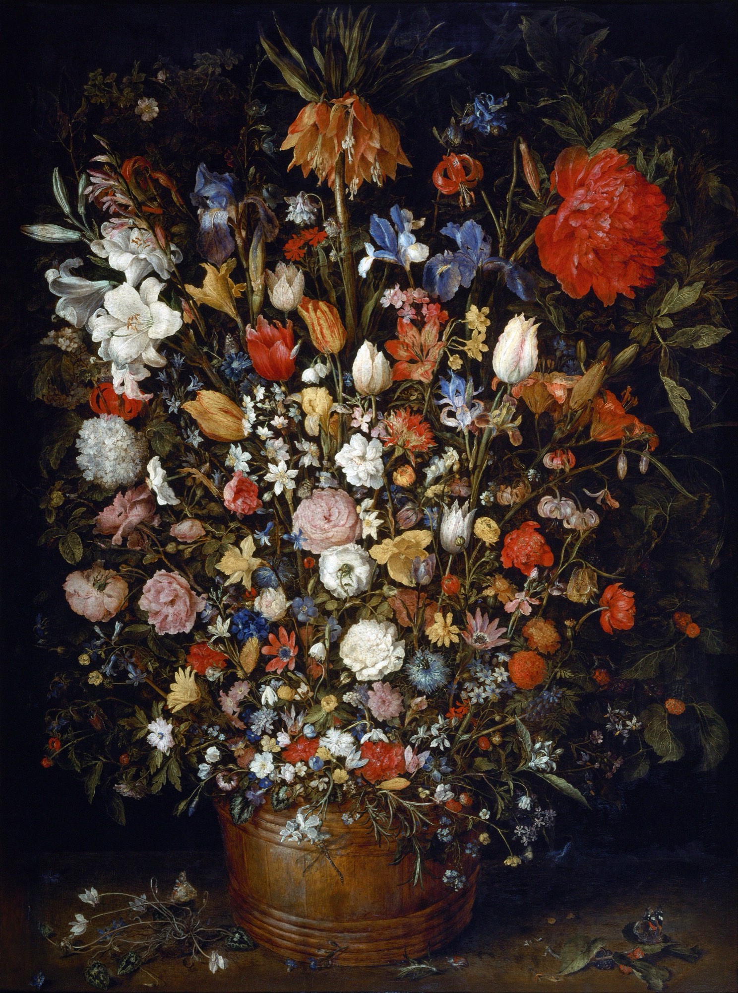 A large bouquet of many kinds of flowers in a round wooden tub on a table, with a few fallen flowers and butterflies on the tabletop.