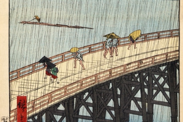 A Japanese woodblock print of a long wooden bridge in heavy rain, with a few walkers under hats and umbrellas and a raft on the river beyond.
