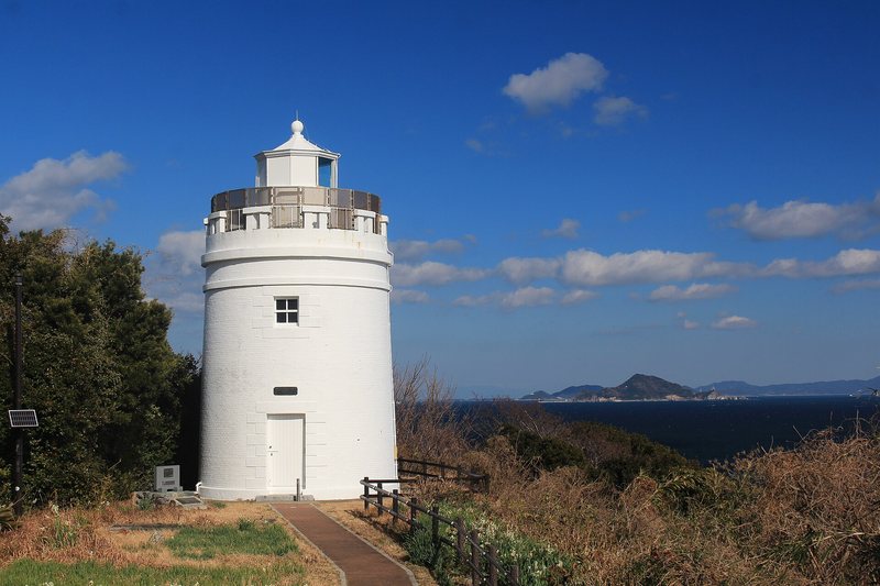 A white lighthouse above the sea with an island on the horizon
